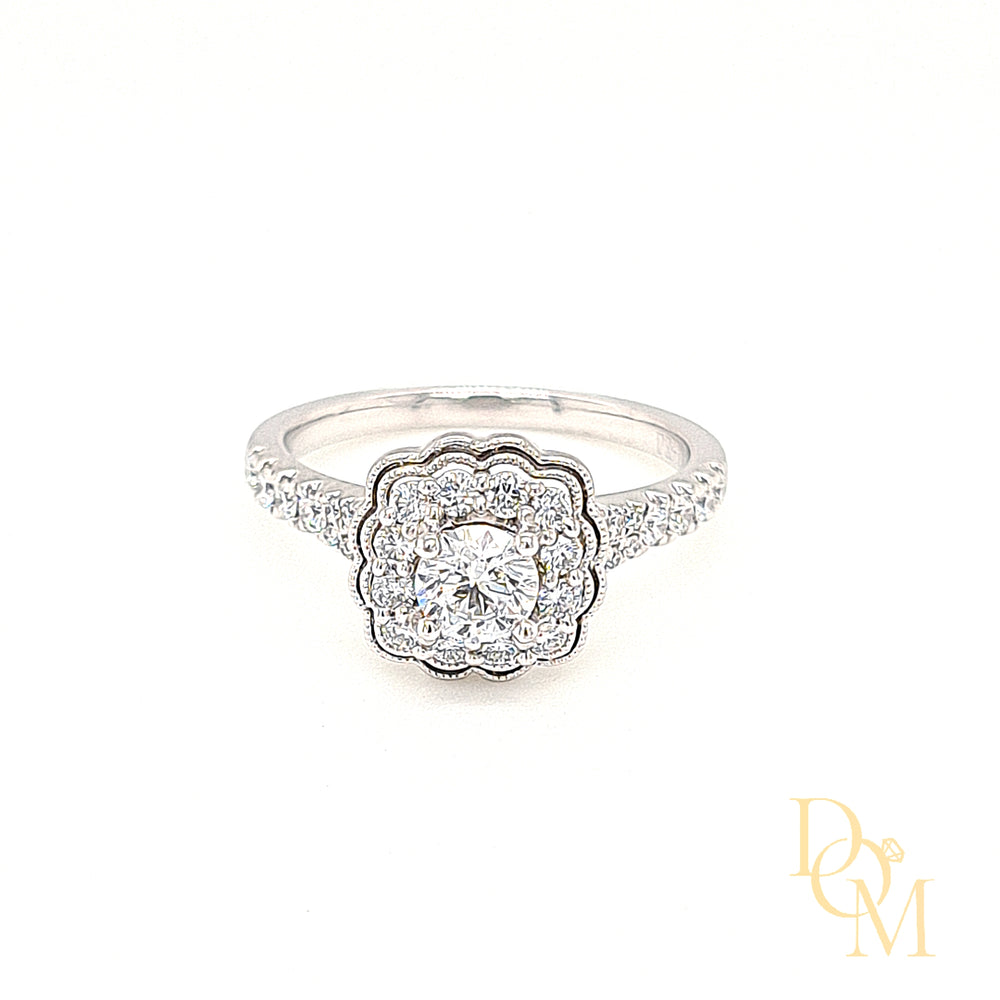 A round diamond in a four claw setting surrounded by a cluster of pavé-set diamonds with a scalloped edge with claw-set diamond shoulders