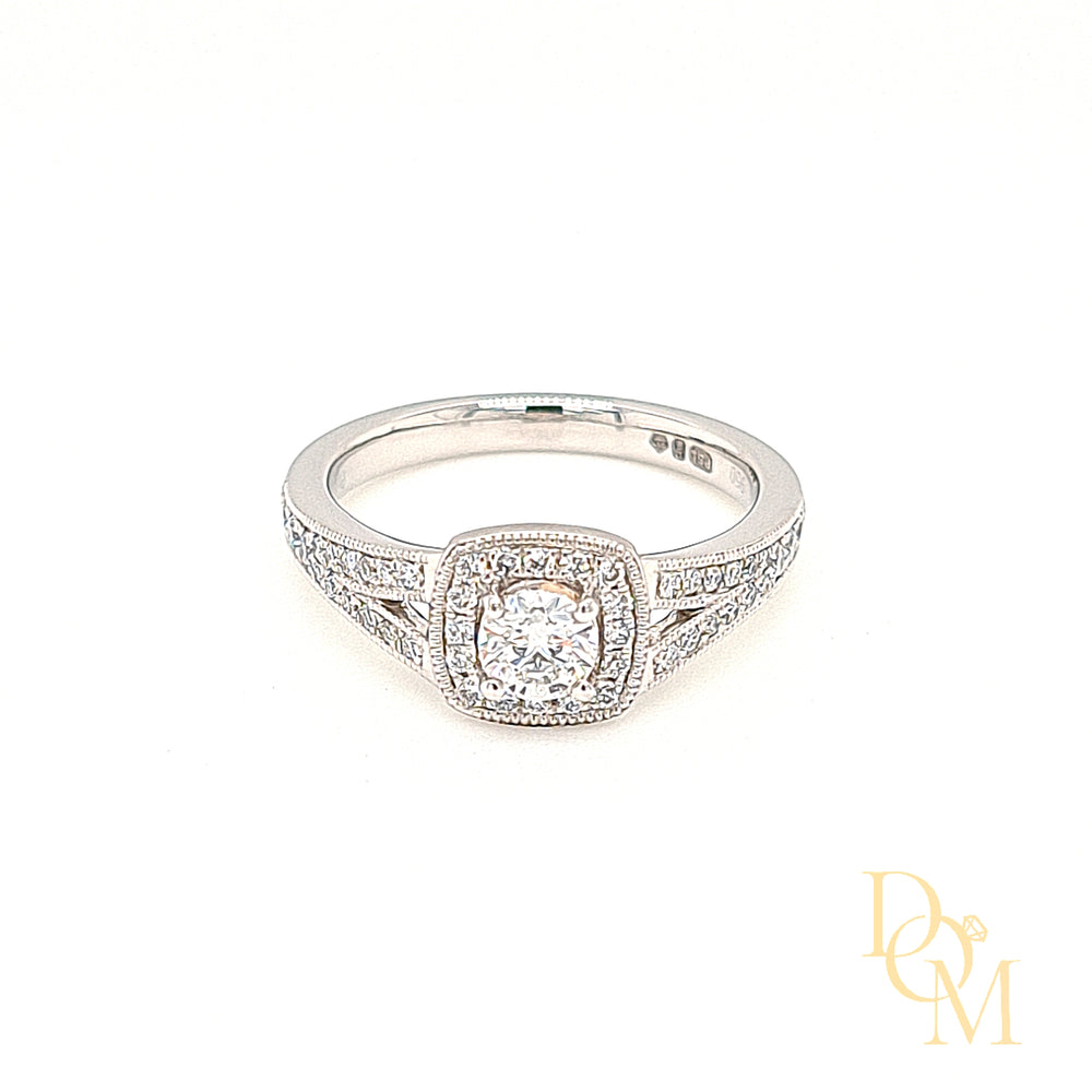 round diamond in centre surrounded by a cushion shaped halo cluster of pavé-set diamonds with spilt diamond shoulders