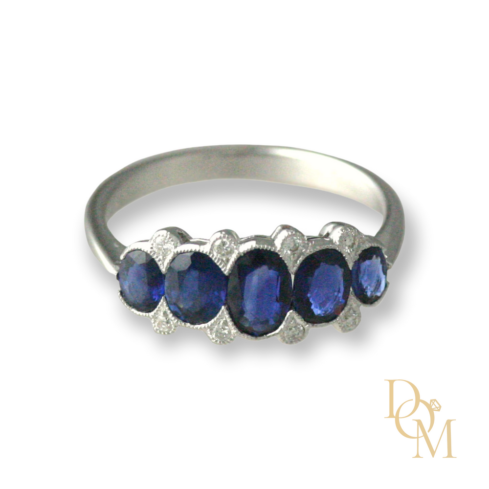 5 graduating oval sapphires in a scalloped edge setting with a round diamond on the outer edge on either side  between each sapphire. set in white gold