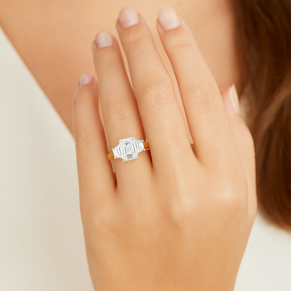 Close-up of emerald-cut lab grown diamond held by talon claws in a white gold setting, flanked by trapezoid cut side diamonds on a tapered yellow gold band, modelled on a ladies ring finger
