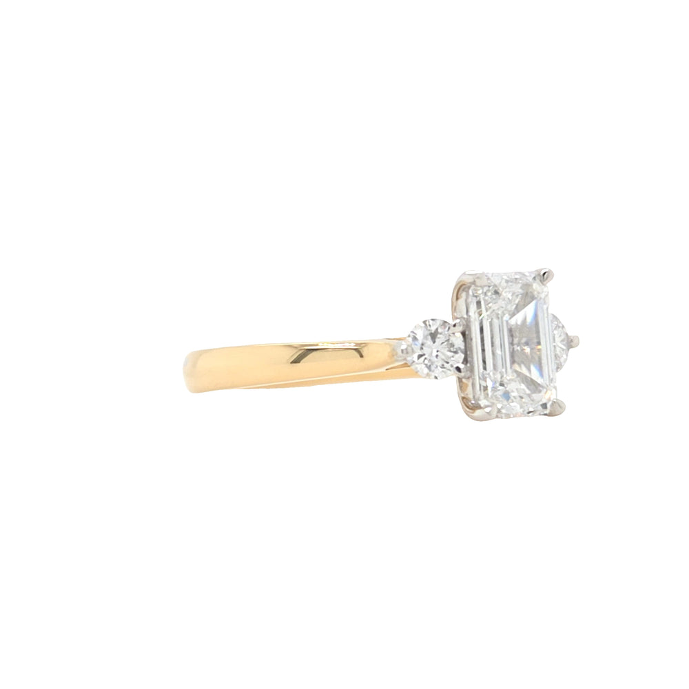 side view of An emerald-cut and two round brilliant-cut lab grown diamonds in a platinum claw setting with a tapered yellow gold shank