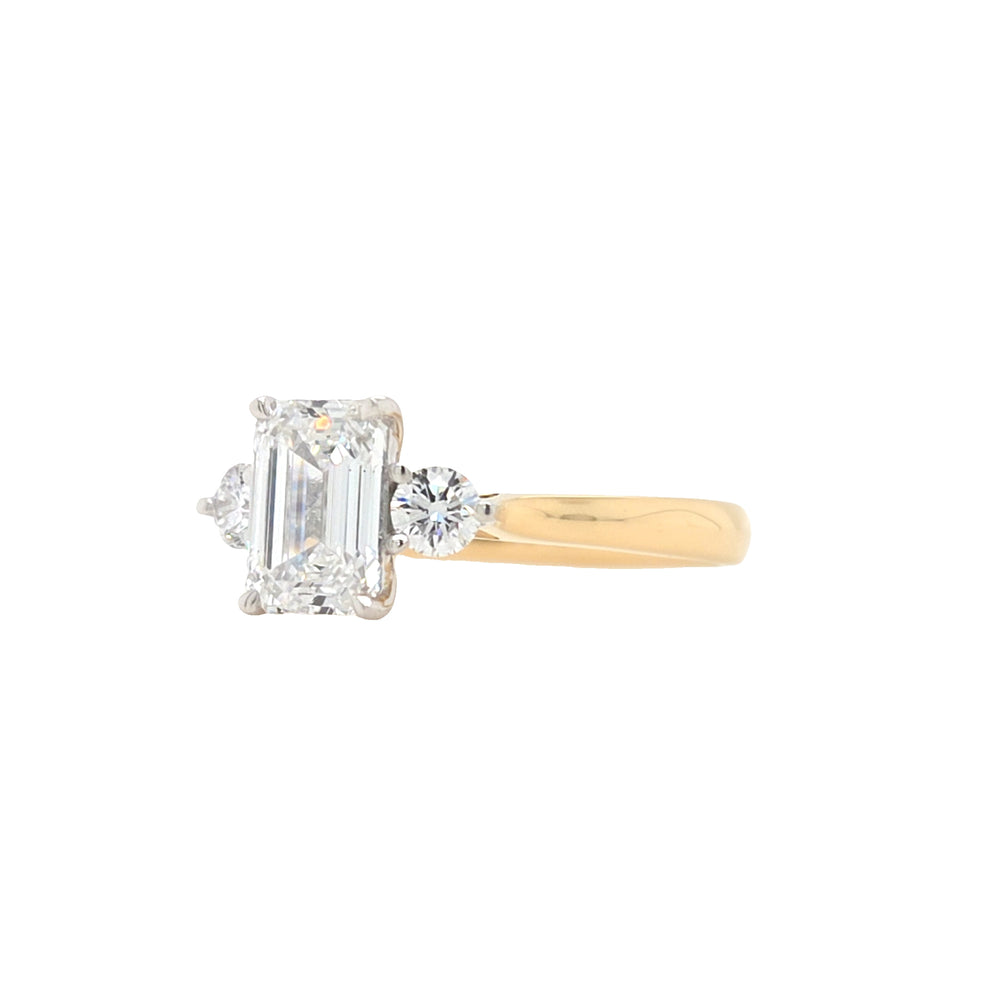 side view of An emerald-cut and two round brilliant-cut lab grown diamonds in a platinum claw setting with a tapered yellow gold shank
