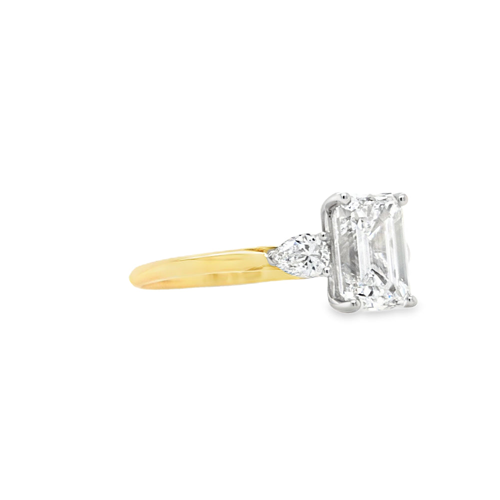 Side view of An emerald-cut and two brilliant-cut lab grown diamonds all in a platinum claw setting with a yellow gold shank