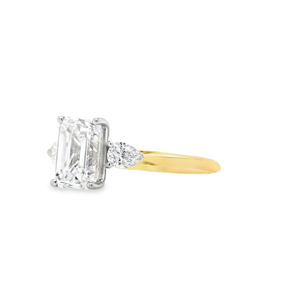 side view of An emerald-cut and two brilliant-cut lab grown diamonds all in a platinum claw setting with a yellow gold shank