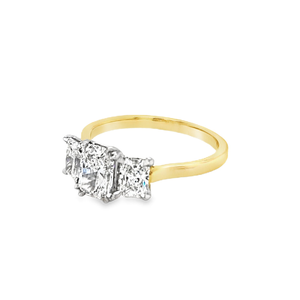 View from the front side of Three stone radiant cut lab grown diamond ring. The larger centre is set with four double eagle claw and the smaller sides are set with four eagle claws. The ring features a plain and tapered yellow shank and the setting is in platinum