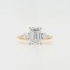 An emerald-cut and two brilliant-cut lab grown diamonds all in a platinum claw setting with a yellow gold shank