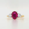 18ct yellow gold and platinum three-stone ring featuring an oval lab grown ruby with round brilliant lab diamond sides on white background.