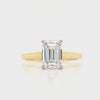 Emerald cut lab grown diamond in a four claw platinum setting with plain yellow gold band with hidden halo under setting