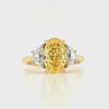 A yellow gold three-stone ring featuring a large oval-cut fancy yellow center stone and two smaller half-moon side stones, set on a plain white background.