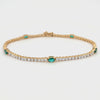 Gold tennis bracelet with oval lab grown emeralds and round lab grown diamonds on a white background
