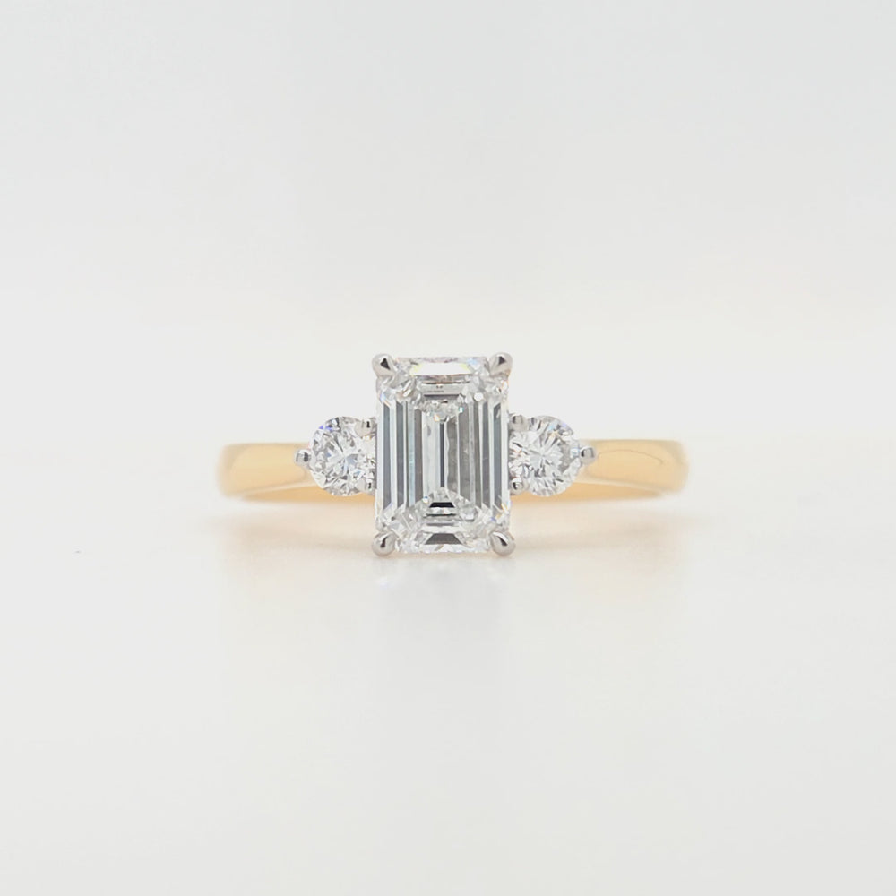 
                
                    Load and play video in Gallery viewer, An emerald-cut and two round brilliant-cut lab grown diamonds in a platinum claw setting with a tapered yellow gold shank
                
            
